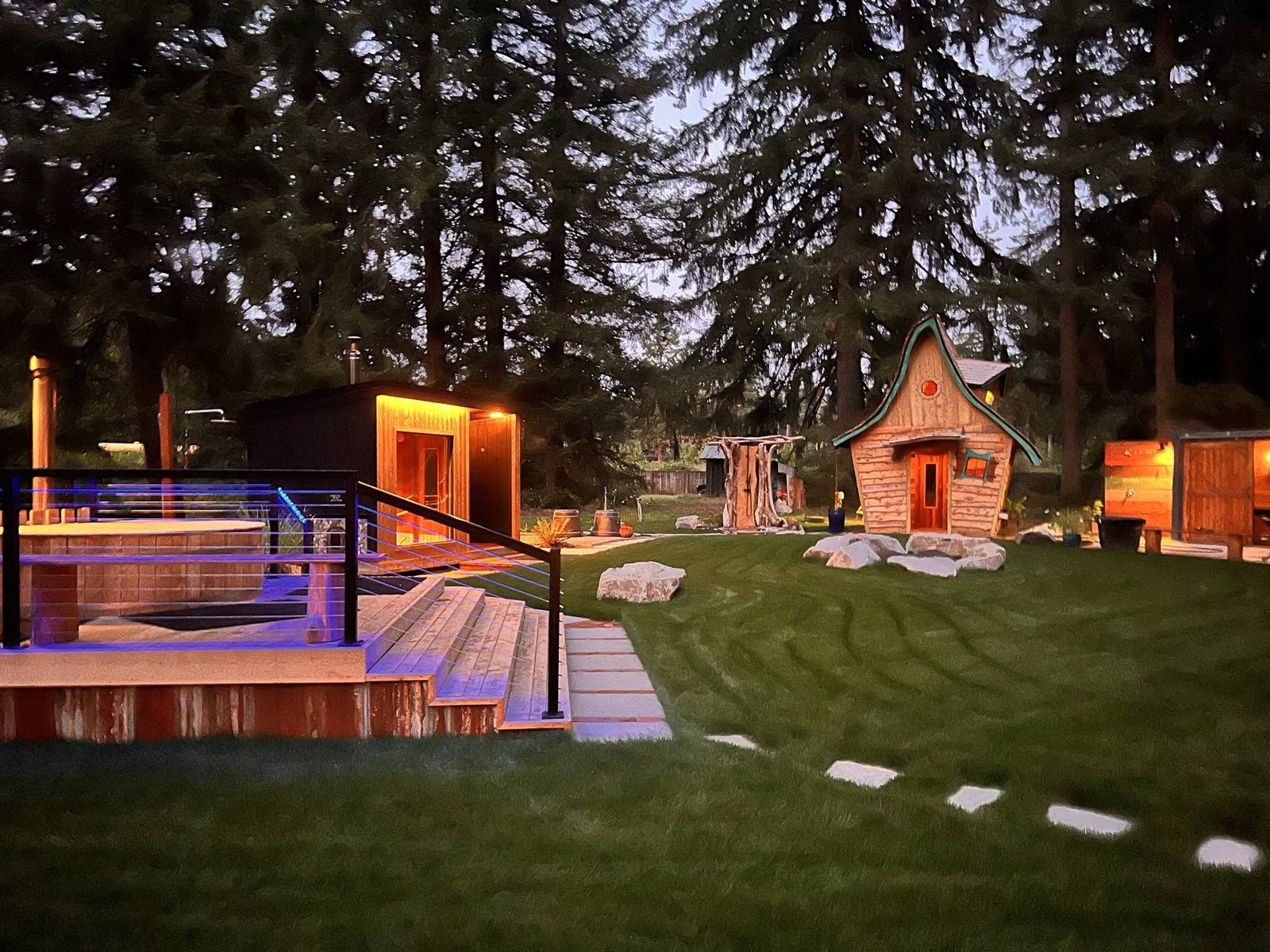 The lawn at dusk with the soaking deck, stepping stones, and the hand-built sauna