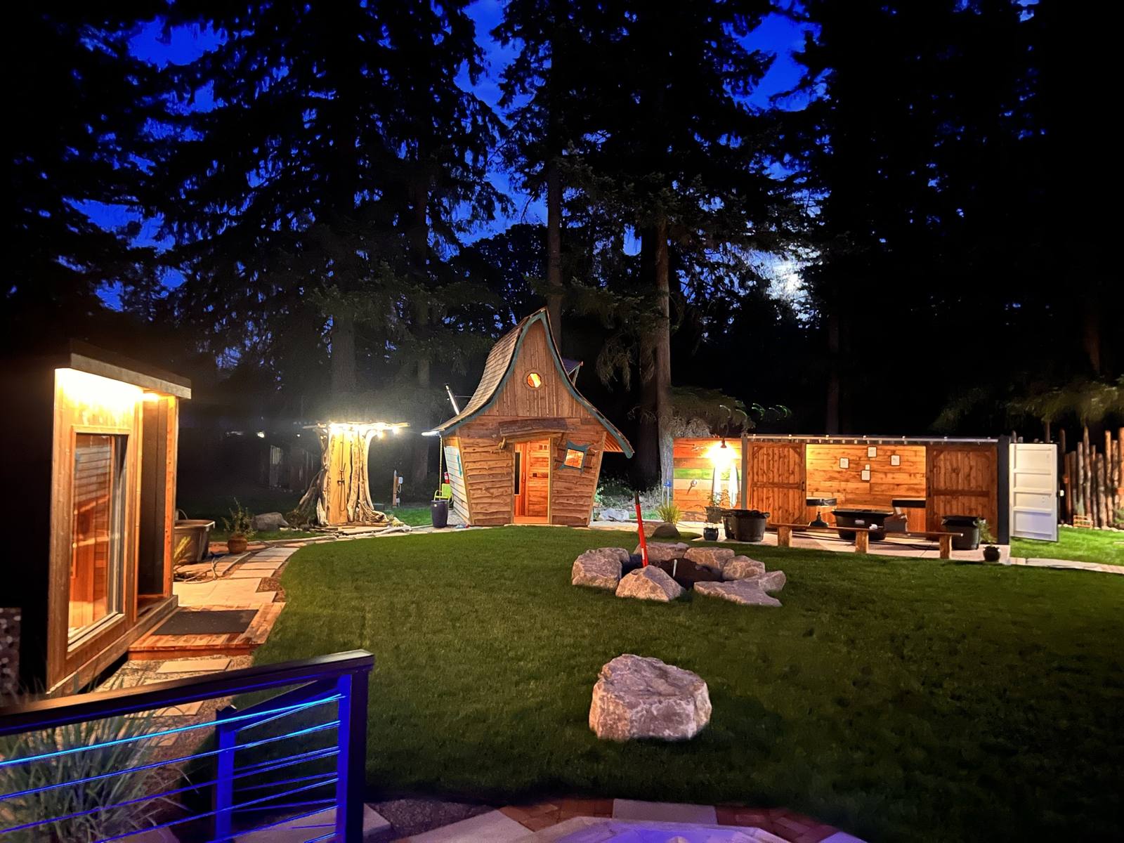 The KickBack grounds at twilight — saunas, plunge deck, and firepit lawn under the firs