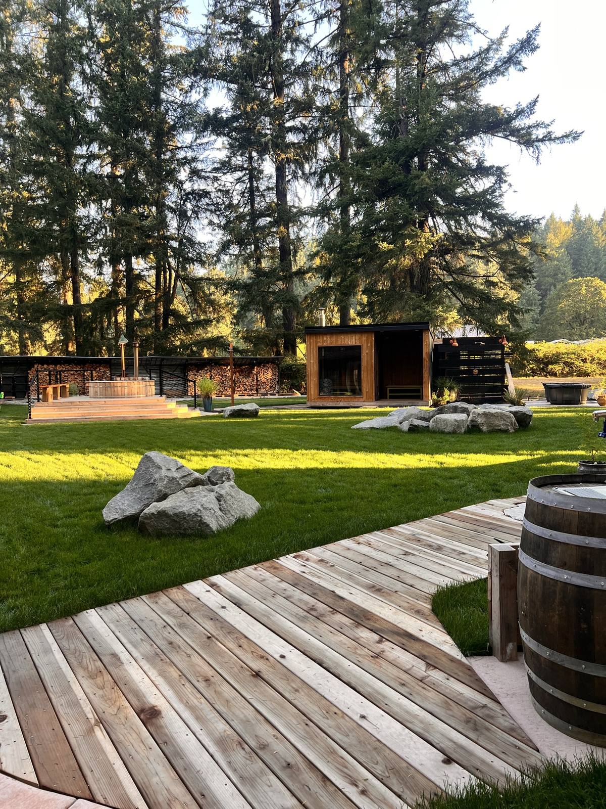 The modern cedar sauna at golden hour, boardwalk crossing the lawn