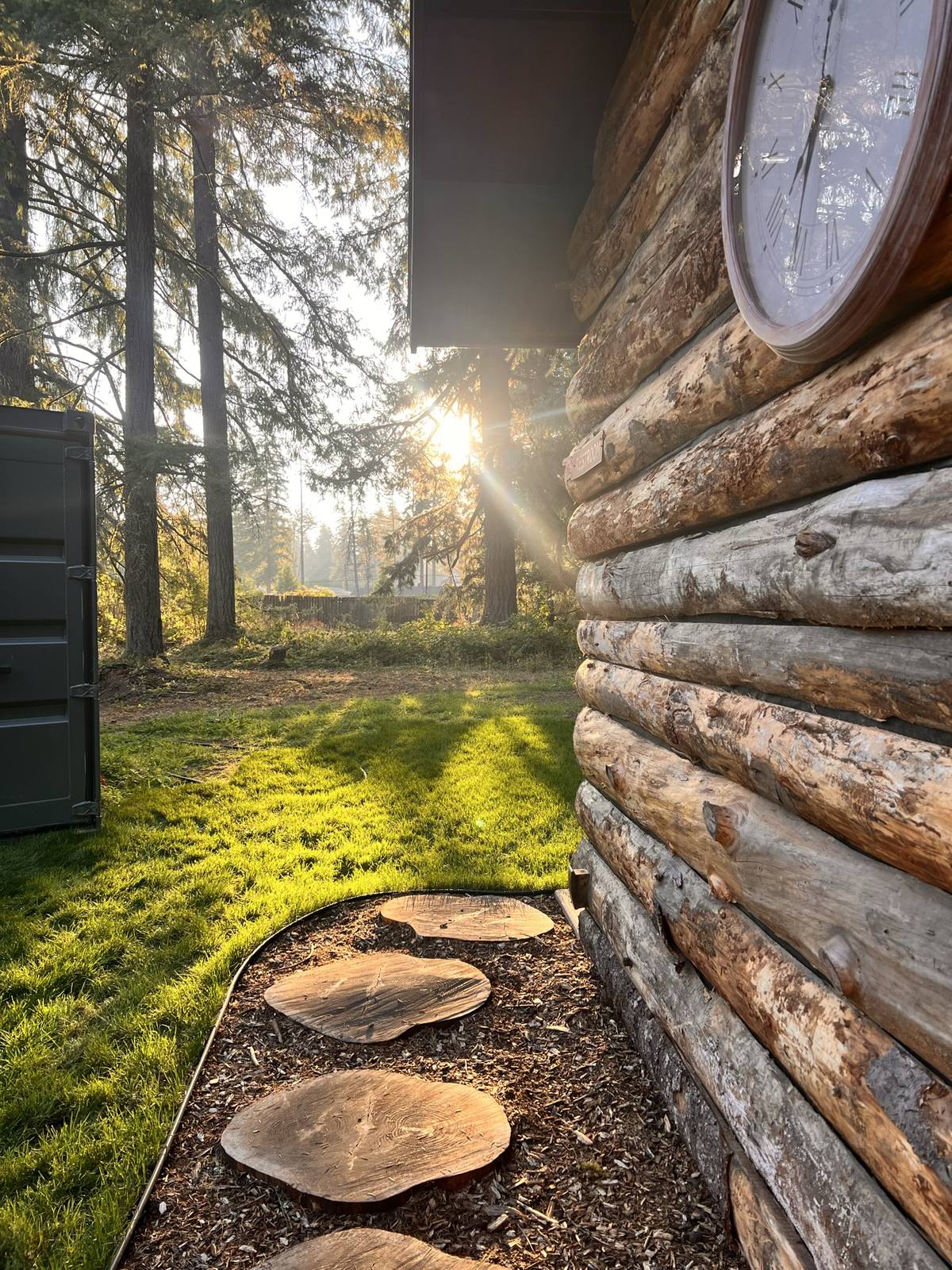 Sun breaking through the trees along the log wall and wood-round path