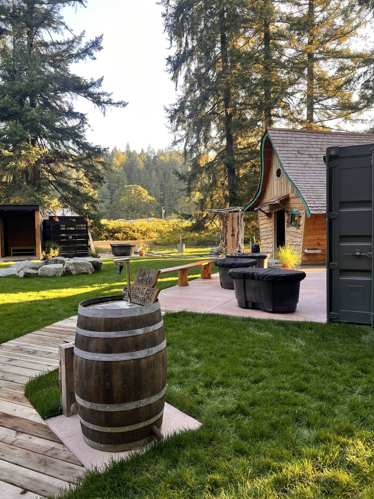 Bottle-fill water barrel with the plunge tubs and hand-built sauna beyond